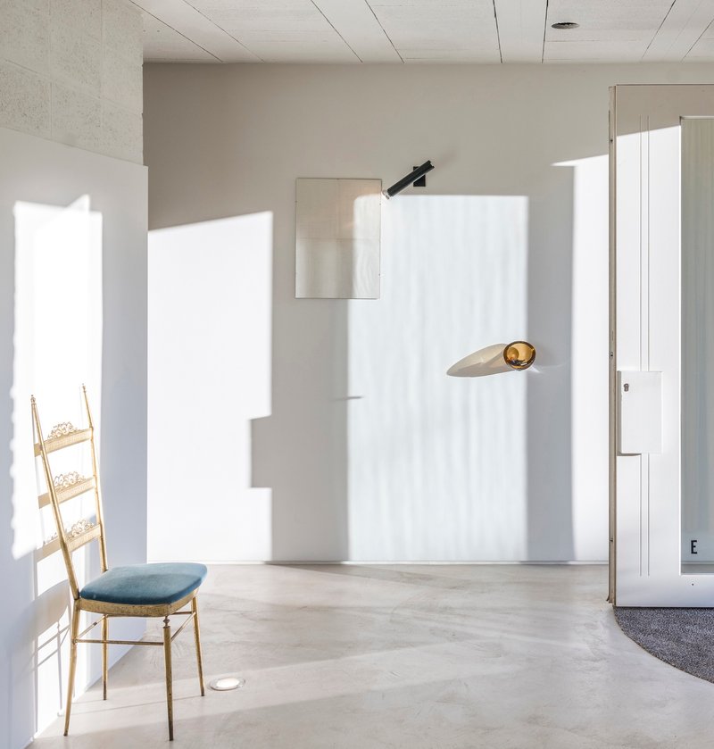 Interior room with concrete floor, timber ladder chair and sharp sunlight patterns across white walls
