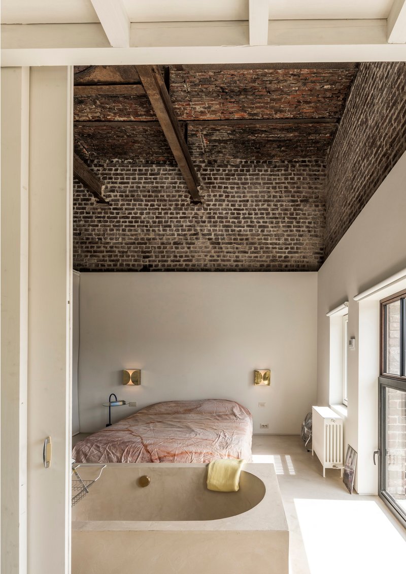 Bedroom with exposed brick ceiling vault, timber beams, and raised platform bed framed by white walls