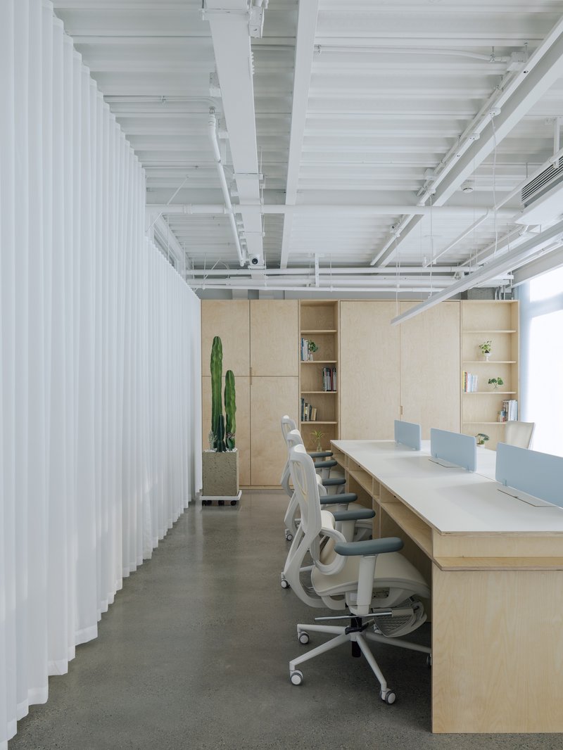 Open workspace with exposed white joists, plywood desk units, and a vertical white slat partition