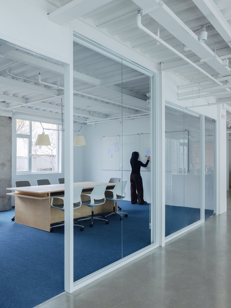 Glass-walled conference room with blue carpet and a figure writing at a whiteboard