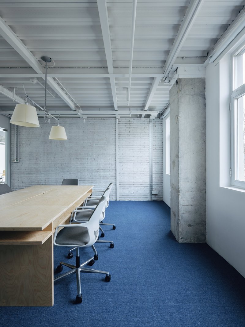 Meeting space with painted white brick wall, exposed concrete column, and blue carpet flooring
