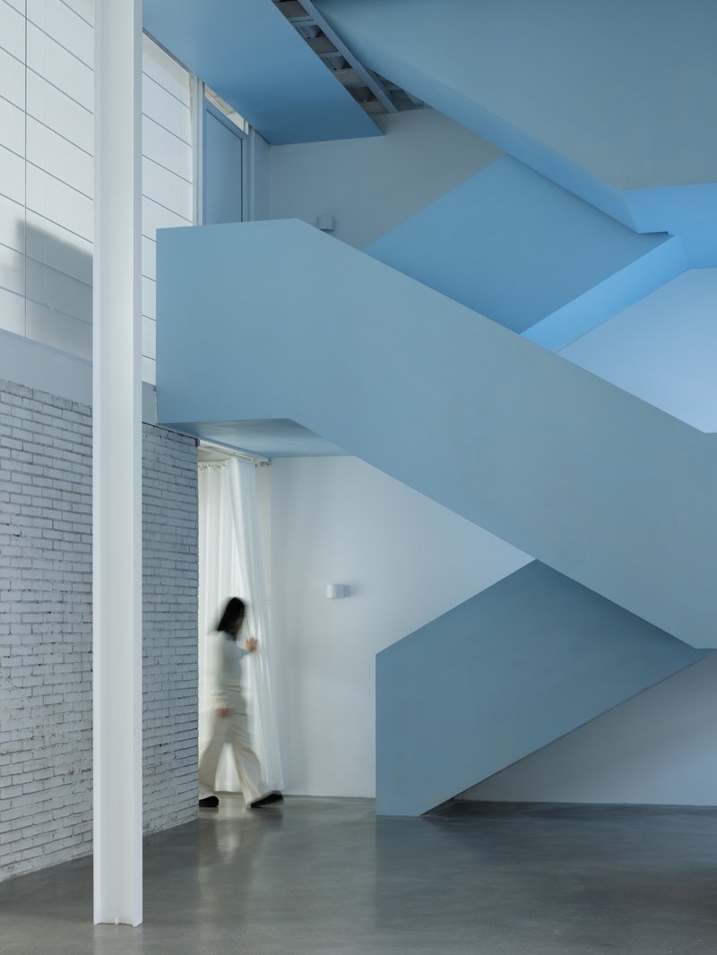 Cantilevered blue staircase with a figure in motion passing beneath the folded geometry