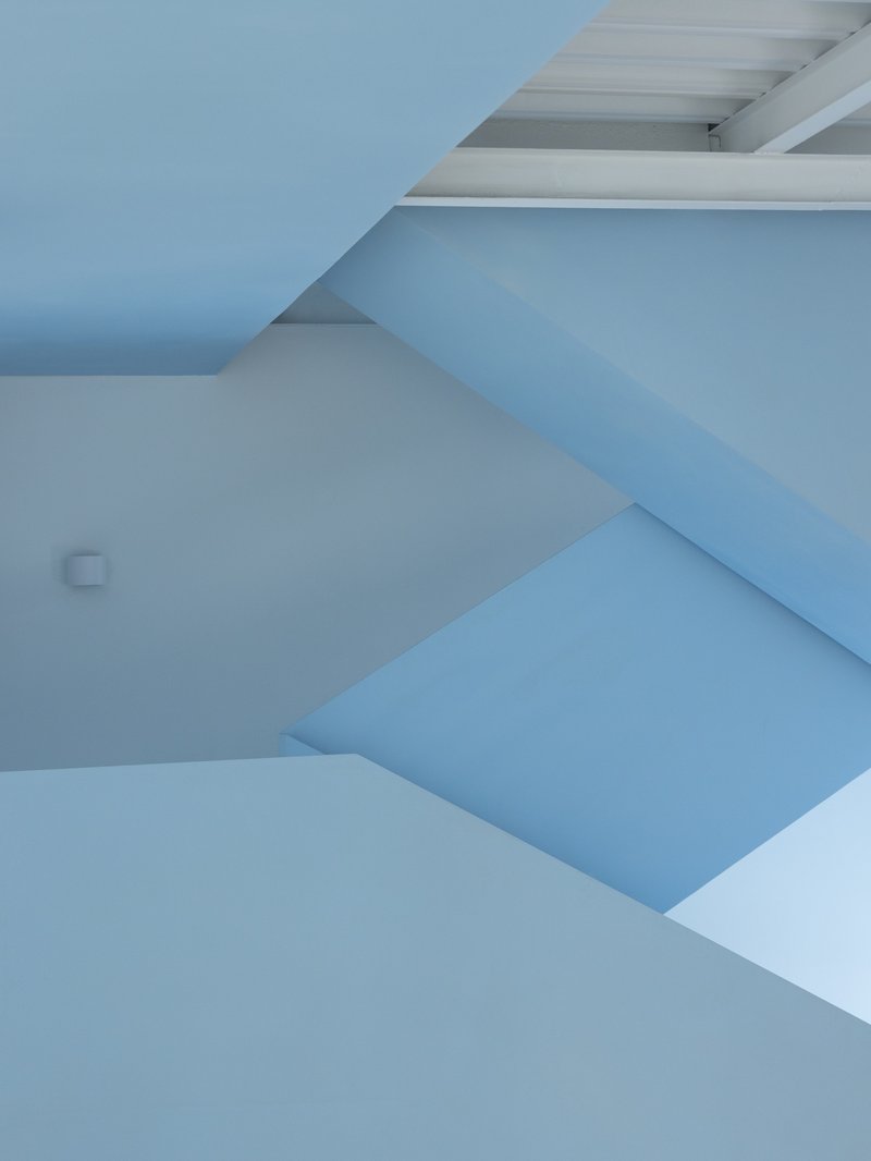 Close view of the folded blue stair soffit and white wall planes under daylight