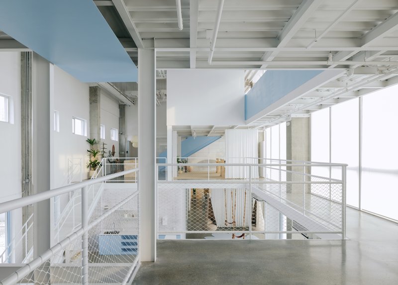 Double-height interior with white metal mesh railings and exposed timber joist ceiling over polished concrete floors