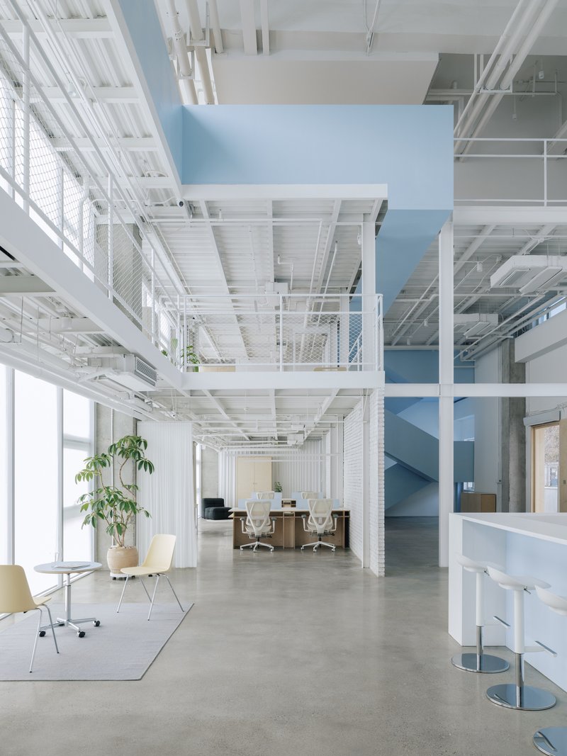 Open office space with white painted steel structure, mesh guardrails and a pale blue stairwell volume