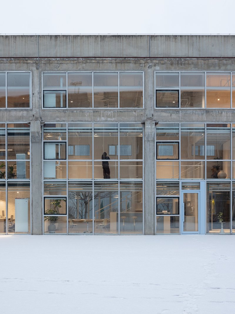 Concrete frame facade with gridded glass windows and a figure standing on the second floor