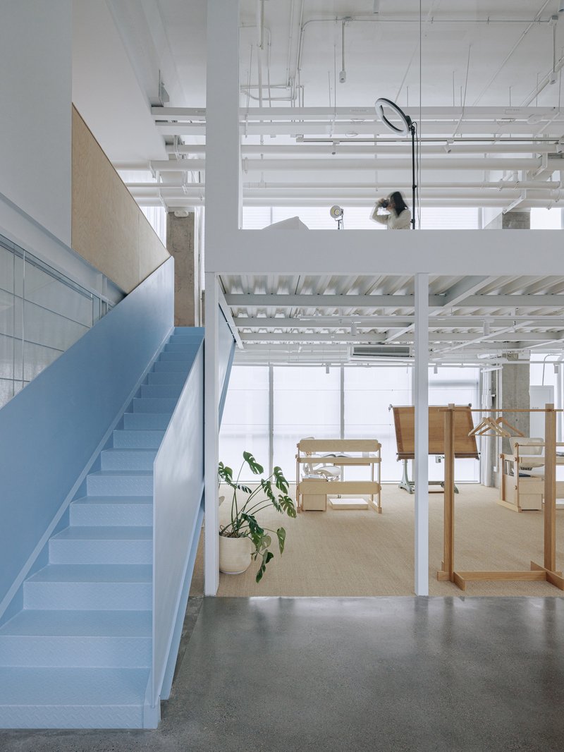 Interior view of pale blue staircase with exposed ceiling infrastructure and potted plant below