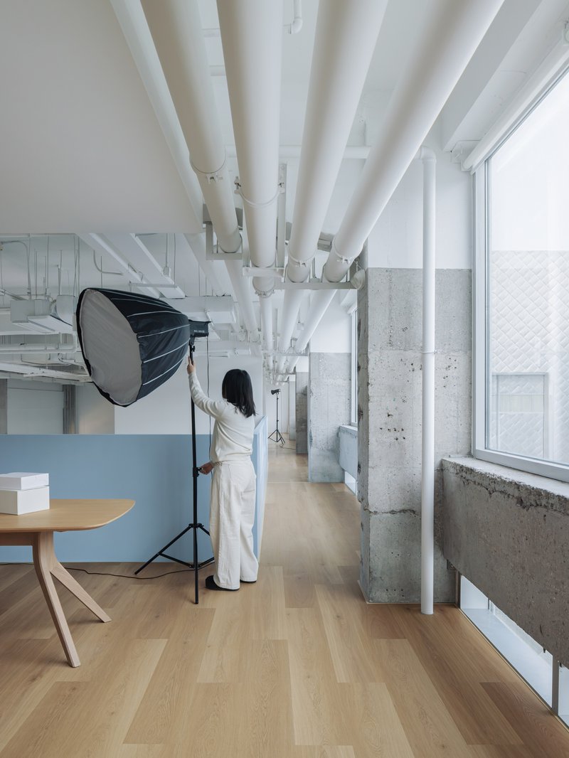 Corridor with radiating white structural beams overhead and person adjusting studio lighting near concrete columns