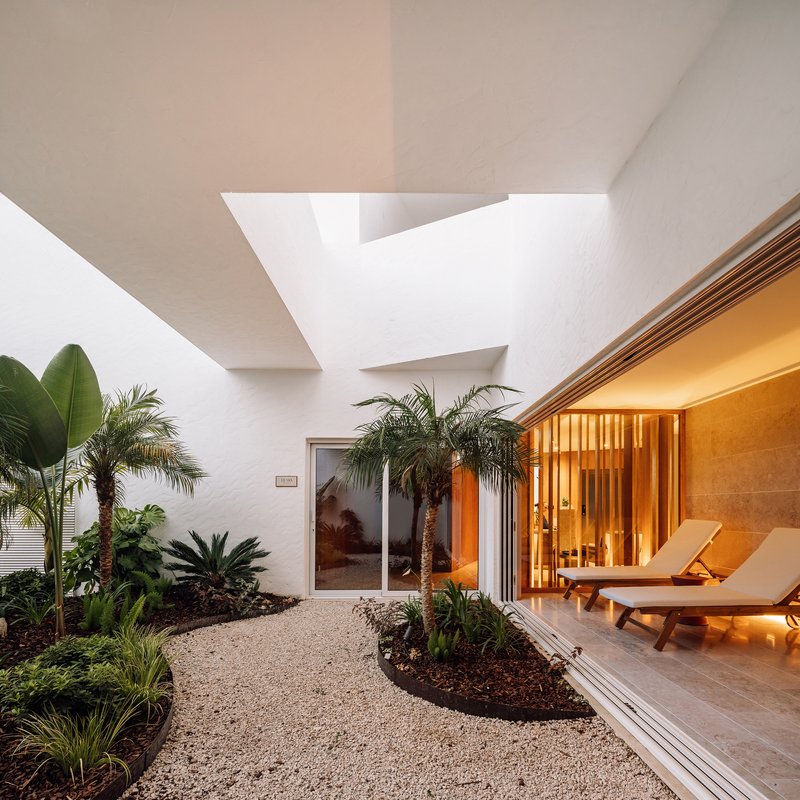 Interior courtyard with gravel pathways, tropical palms, and timber-screened spa room illuminated at dusk