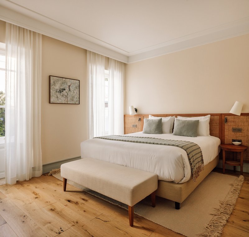 Bedroom with timber headboard, knotted pine flooring and sheer curtains filtering daylight