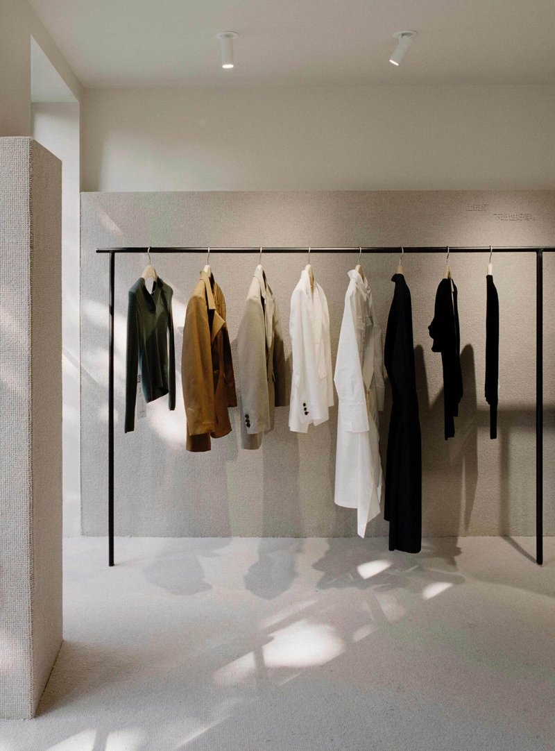 Black clothing rail with hanging garments in natural light against textured plaster wall