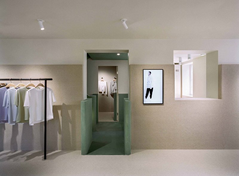 Retail interior with green plaster portal framing a corridor and clothing rack along textured beige walls