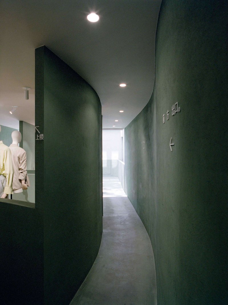 Curved green plaster wall forming a passage with recessed lighting overhead