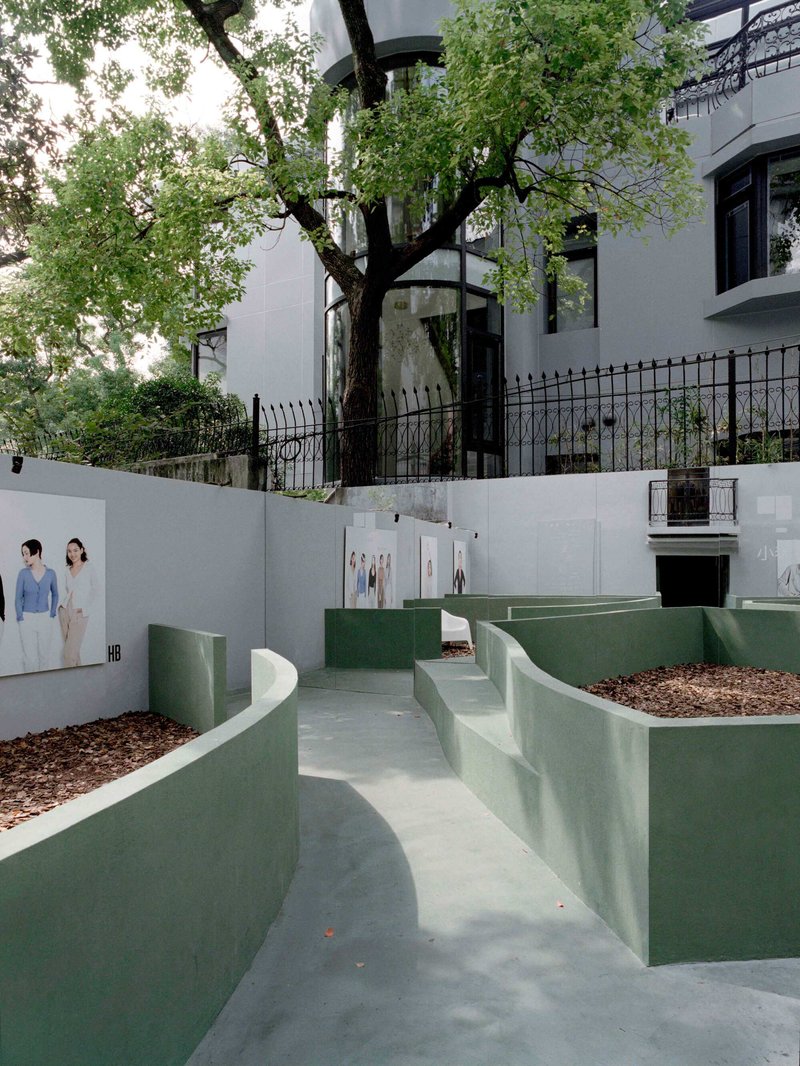 Curving sage green planters with mulch beds and concrete walkways below a preserved tree