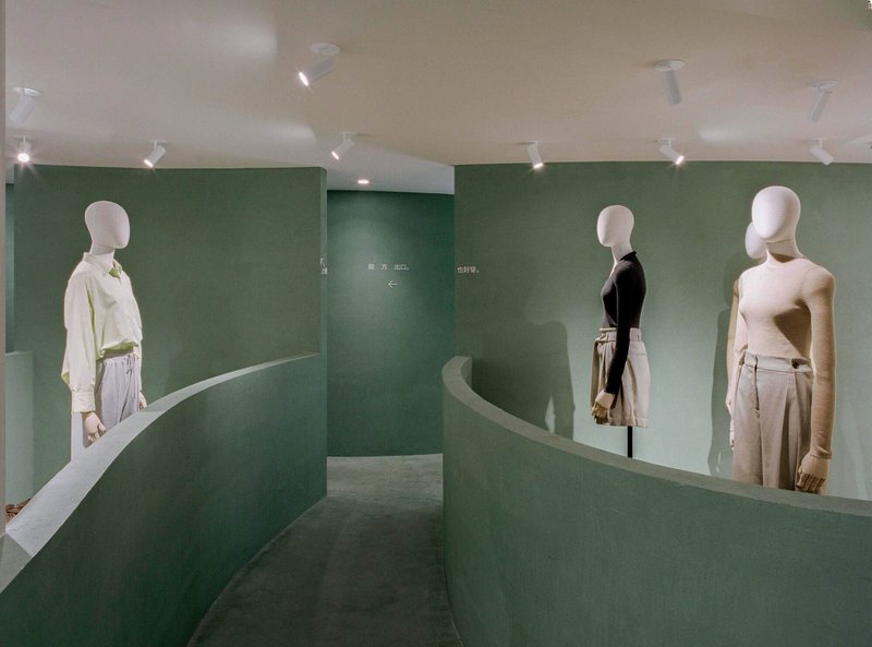 Interior retail space with curving green partition walls and white mannequins displaying clothing