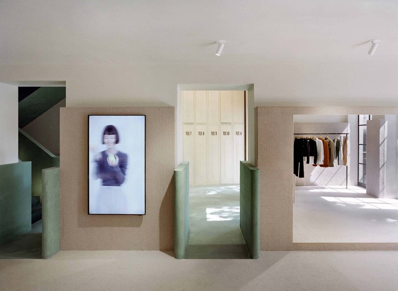 Retail interior with textured beige walls, cream lockers and green staircase under track lighting