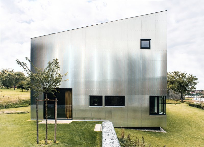 Corrugated metal box volume elevated on the sloping lawn with young trees planted nearby