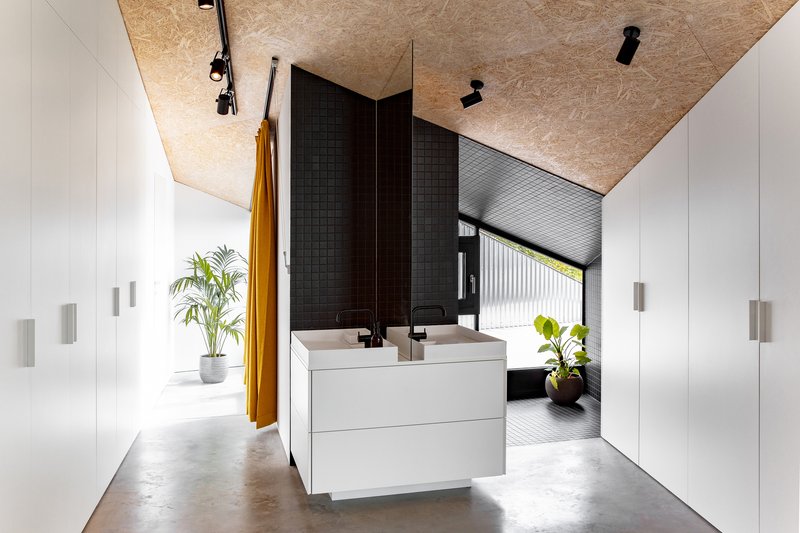 Bathroom vanity beneath an oriented strand board ceiling with black tile partition and orange curtain