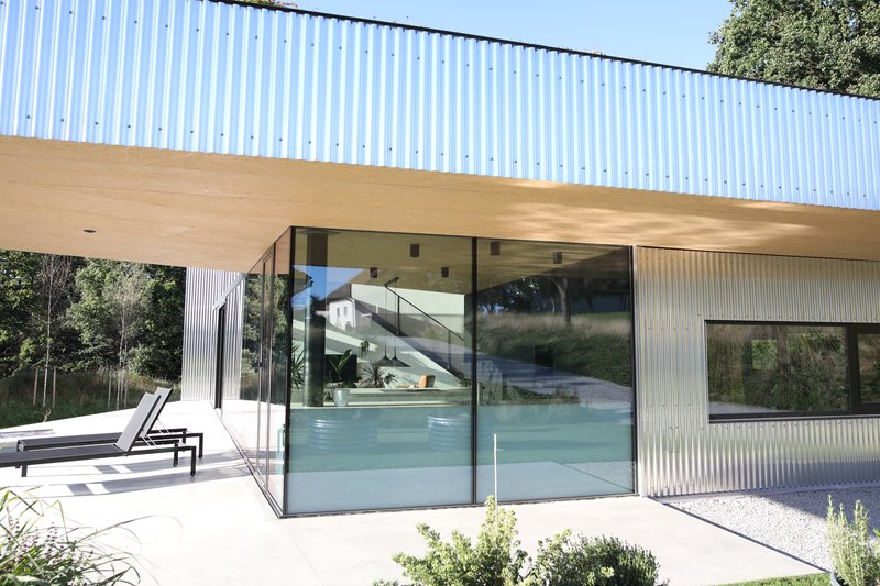Poolside terrace with floor-to-ceiling glass sliding doors below the corrugated metal soffit overhang