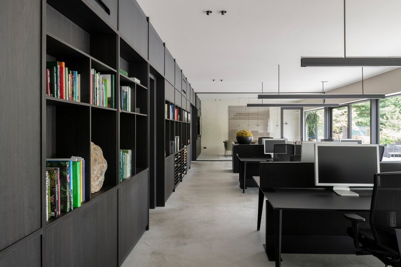 Open office interior with black modular shelving along one wall and workstations beneath linear pendant lights