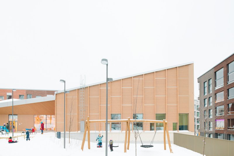 Timber facade with ground-level glazing overlooking a snow-covered playground with children and swings