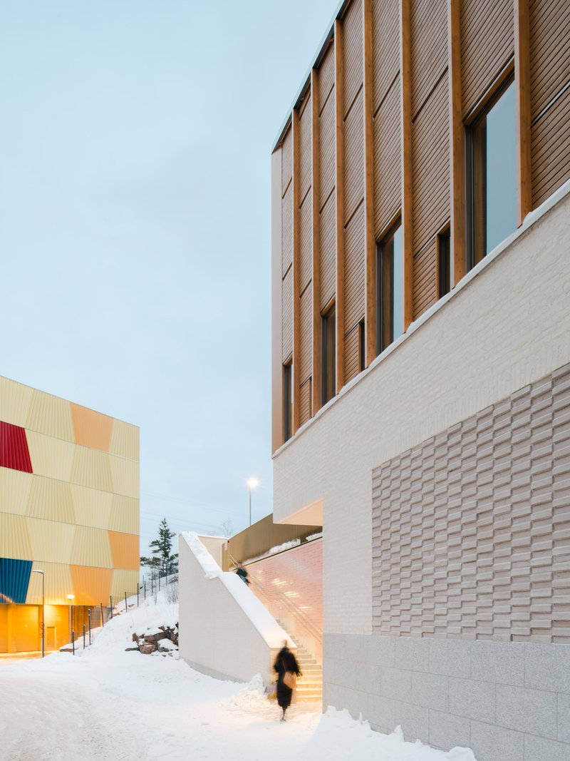 Exterior passage between textured brick base and vertical wood cladding during winter twilight