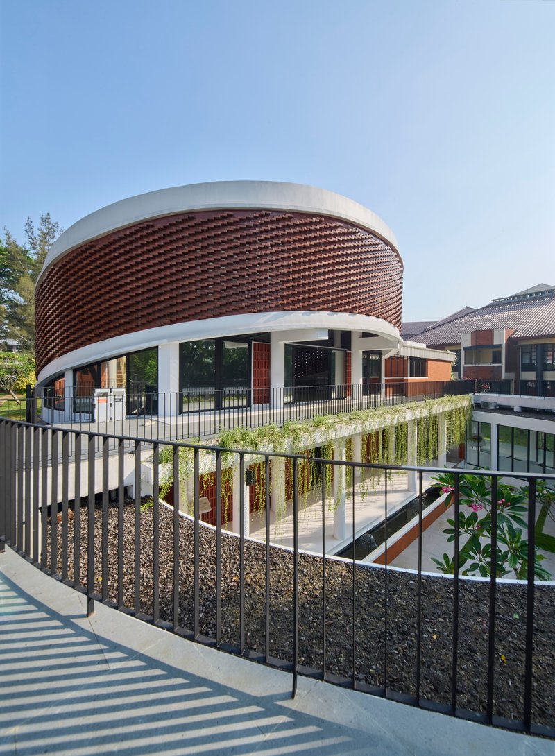 Curved staircase with metal railing leading to planted terrace below cylindrical basketweave brick facade
