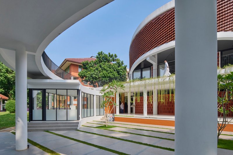 View through white columns framing courtyard with grass strips and person on upper terrace