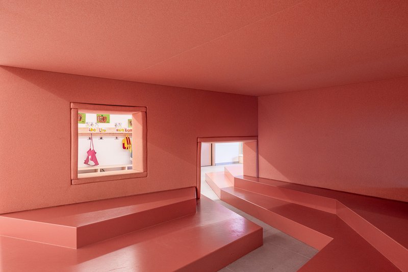 Coral-pink room with built-in stepped seating platforms and window openings framing adjacent spaces