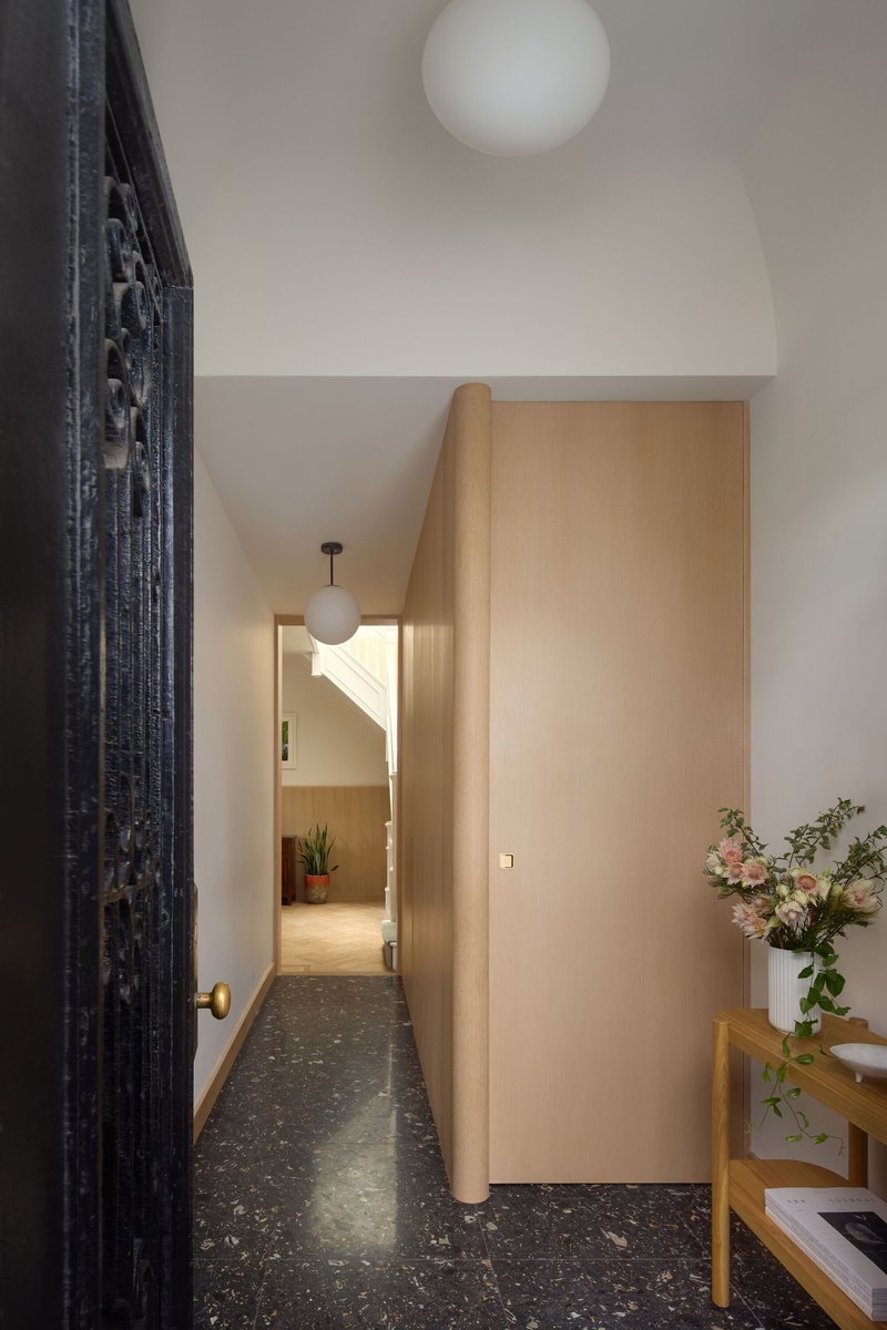 Hallway with terrazzo flooring and timber-clad curved wall leading to a lit doorway