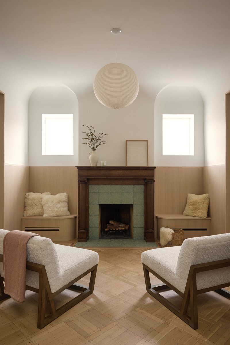 Sitting area with fireplace flanked by built-in benches and arched windows above timber wainscoting