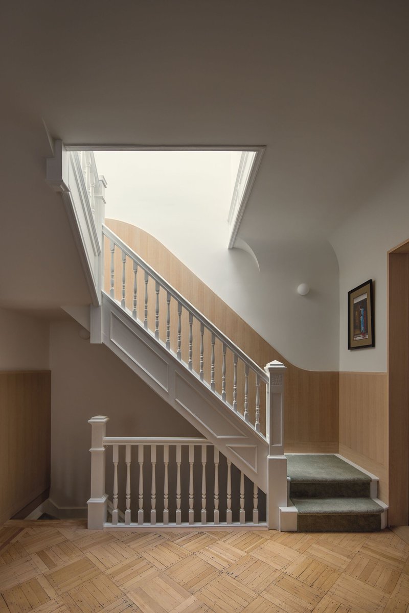 Staircase with painted balustrade and timber handrail beneath a skylight with natural daylight
