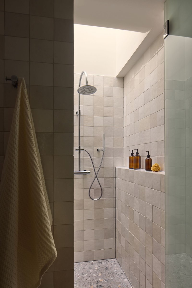 Shower enclosure with white tile walls and skylight casting angular sunlight onto the fixtures