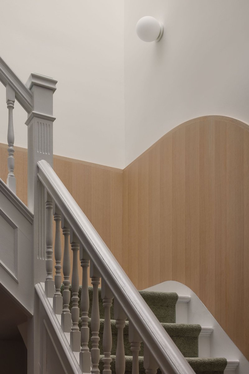 Staircase with turned white timber balusters ascending past a curved oak paneled wall