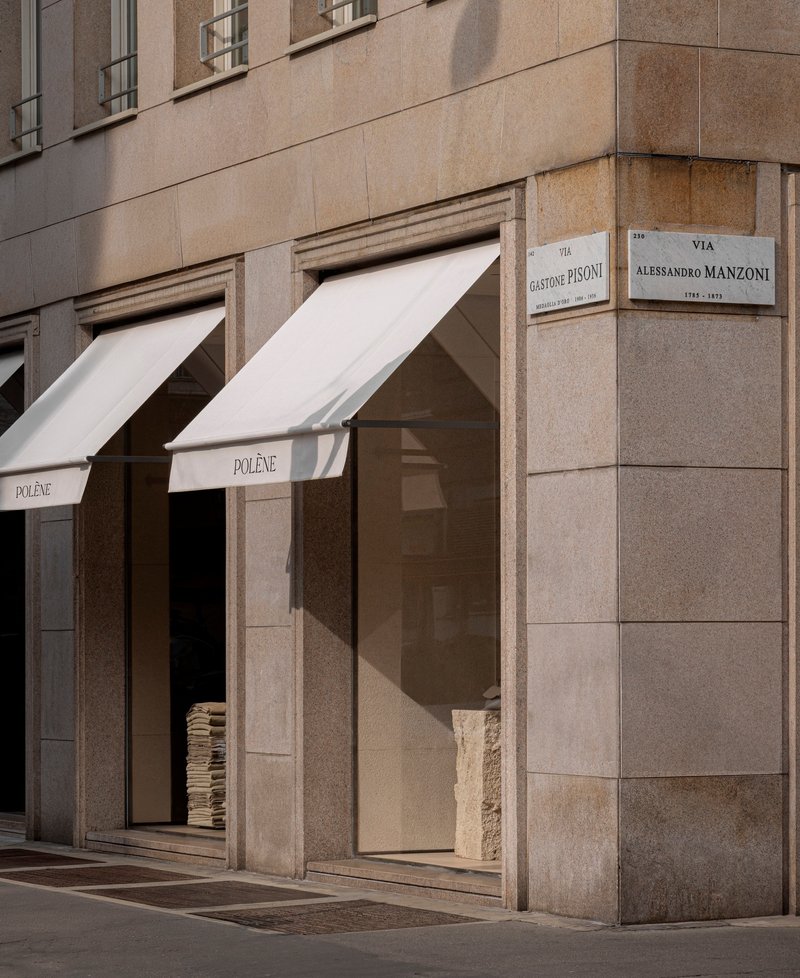 Corner storefront with two white canvas awnings over bronze-framed openings in the stone facade