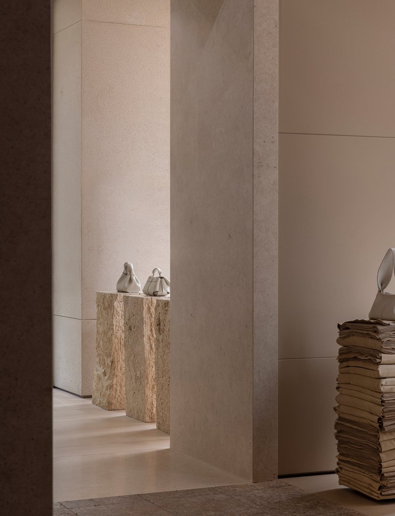 Doorway framed by concrete columns revealing travertine plinths with ceramic vessels in soft light
