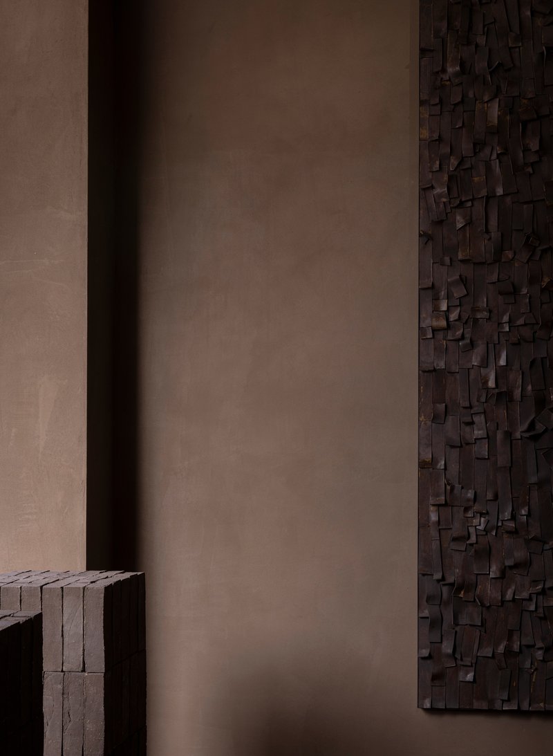 Close-up of dark wooden relief sculpture edge meeting smooth taupe plaster wall in shadow