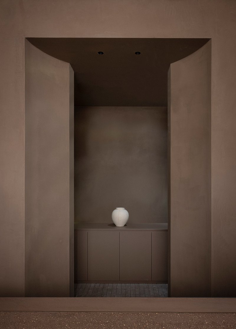 Recessed niche with curved soffit framing a white ceramic vessel on low cabinet