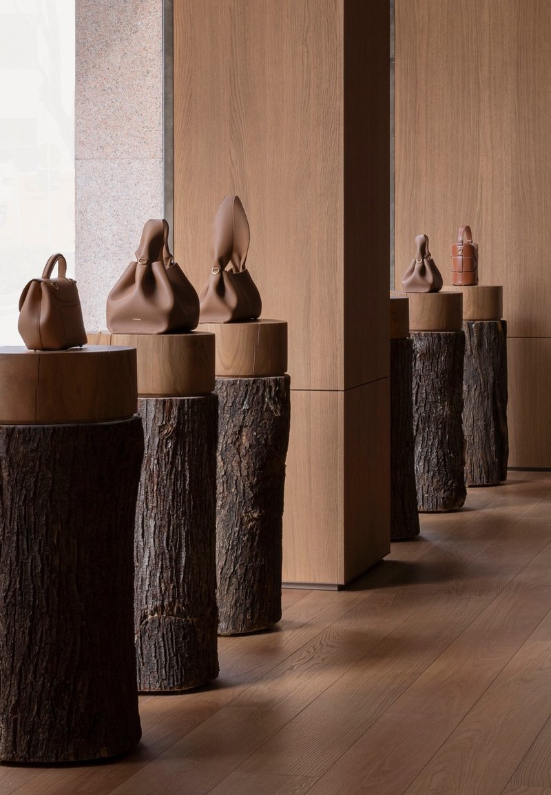 Display plinths combining wood and bark supporting leather handbags against oak paneling