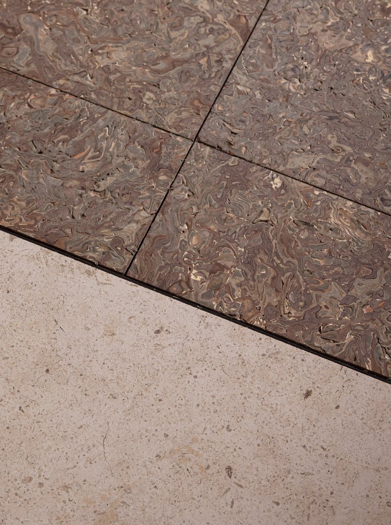 Close-up of marbled terrazzo flooring meeting pale stone tiles at a diagonal joint