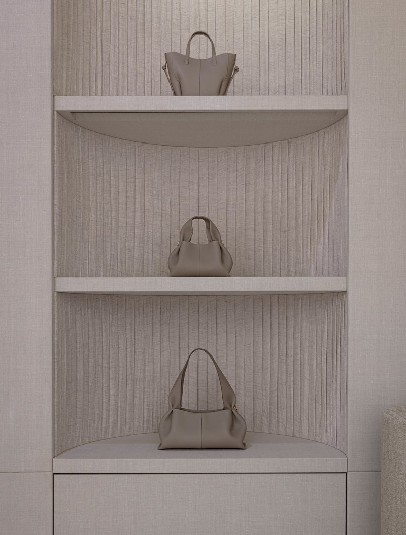 Curved corner shelving niche with fluted linen backing displaying three leather handbags