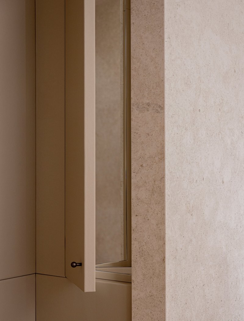 Detail of brass-edged door frame meeting textured limestone wall in warm interior light