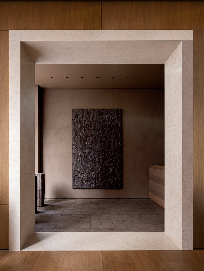 View through beveled stone threshold into a gallery space with textured artwork on rear wall