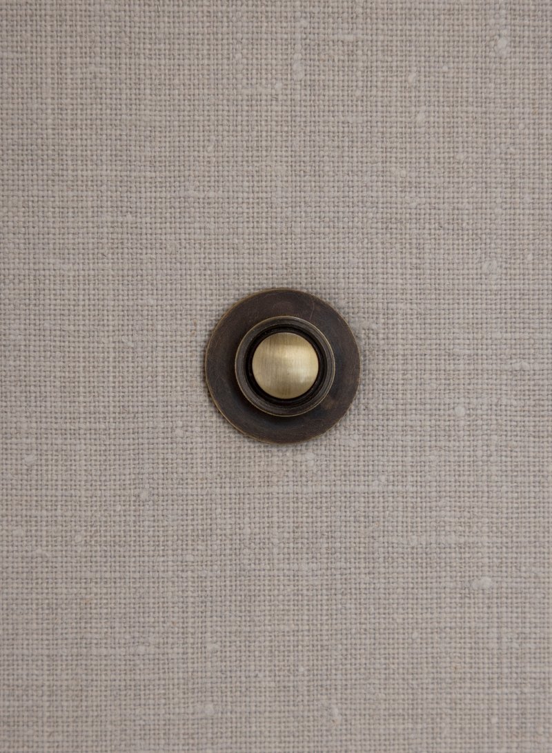 Close-up of bronze doorbell plate with brass button set into textured fabric wall covering