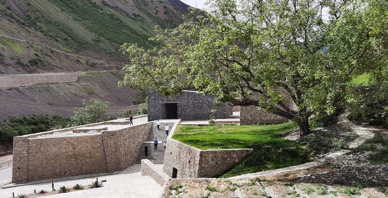 View of the stone walls and lawn terrace framed by a tree against the mountain slope