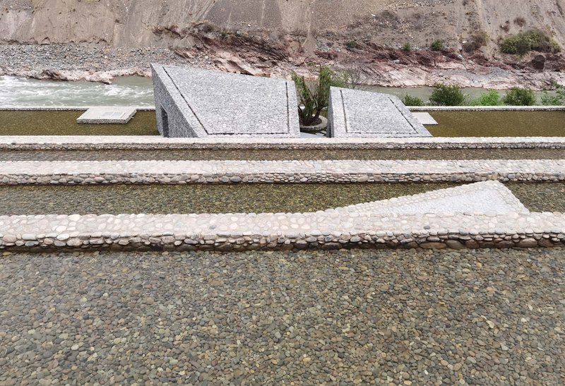 Horizontal water channels lined with white cobbles and stone borders stepping down the hillside