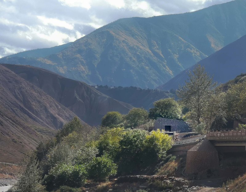 Stone volumes embedded in sloping terrain with trees and ridgelines visible in late afternoon sun