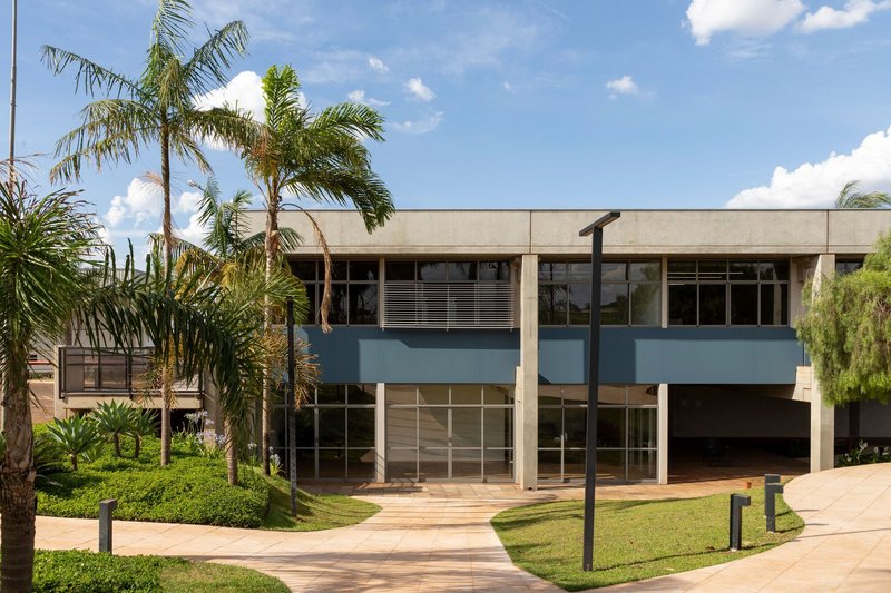Two-story facade with blue horizontal bands and concrete overhangs framed by palm trees and lawn