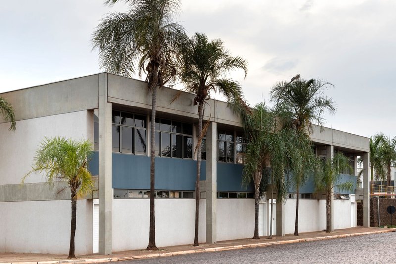 Street view of the concrete and plaster facade with blue window bands behind palm trees