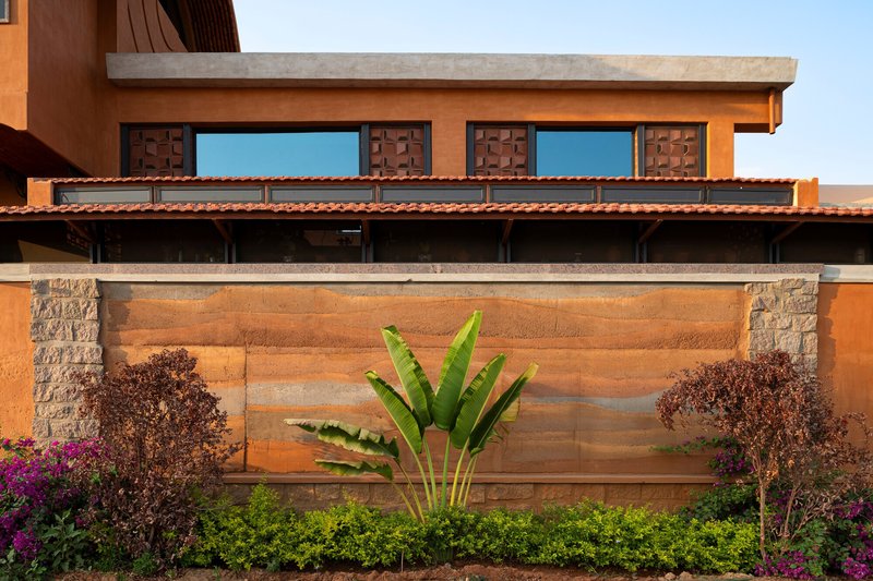 Horizontal banded terracotta wall with stone piers and banana plant against a hedge